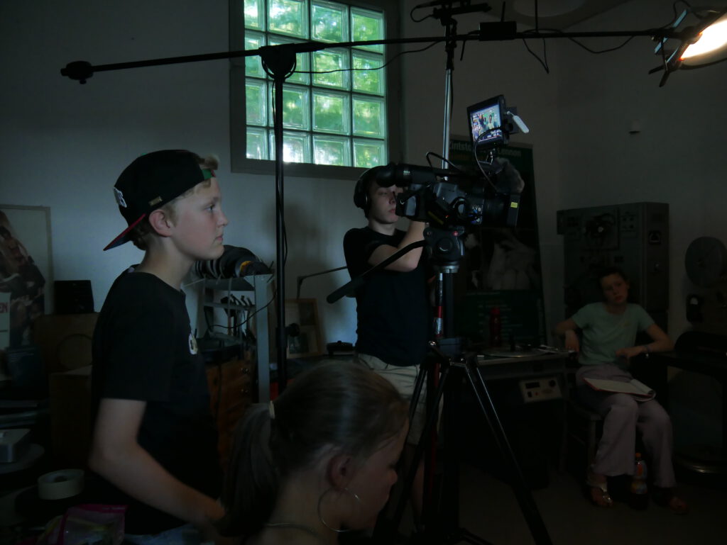Am Set in Bendestorf 2022: Kameramensch, Tonmensch, Regie im Hintergrund mit Spotbeleuchtung in die Szene...